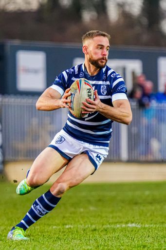 A male athlete running on the field with a rugby ball in his hands