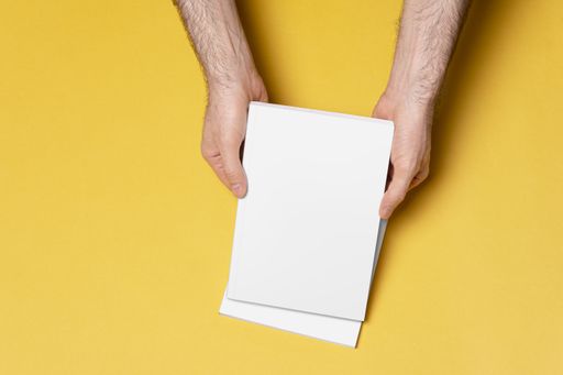 A top view of a man holding empty catalogues with blank covers with space for text on a yellow background