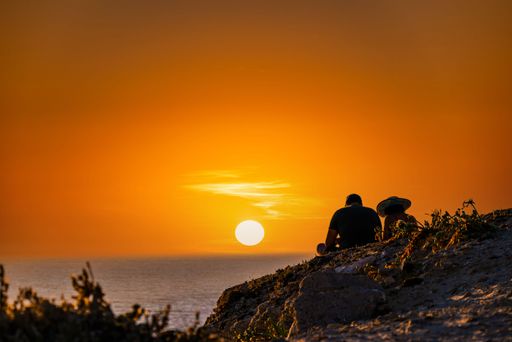 A romantic young couple stands in awe of the beautiful sunset on Barbate beach, near the iconic Trafalgar lighthouse in Cadiz, Spain