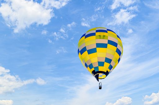 A colorful hot air balloon floating in the air in a cloudy blue sky