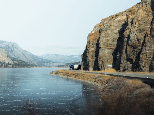 An aerial view of a winding mountain road leading to a stunning lake, Okanagan, Canada