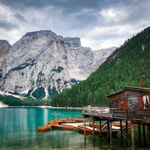 A scenic coastal landscape featuring several small wooden boats moored at the shore with a majestic mountain in the background
