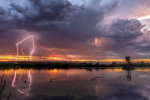 A landscape of a lake with the lightning reflecting on it during the sunset on a stormy evening