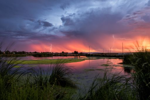 A landscape of a lake with the lightning reflecting on it during the sunset on a stormy evening