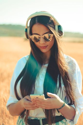 A beautiful young female with sunglasses and headphones changing the music from her phone