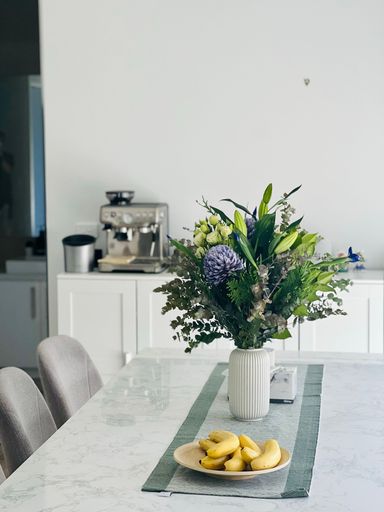 A white table with several yellow ripe bananas and a selection of colorful flowers arranged neatly in a vase next to it