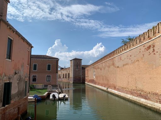 A tranquil canal with a line of boats docked along the side, and a large building in the background