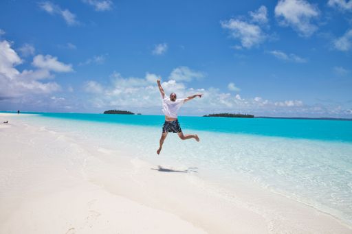 A man jumping in joy on a white sandy beach, his arms stretched out in the air