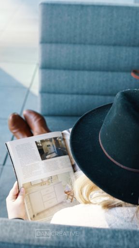 A behind a shoulder shot of an adult female relaxing on the bench and reading a magazine