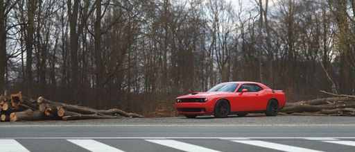 Banner view of red Dodge Challenger SRT Hellcat standing by the road in late autumn landscape.
