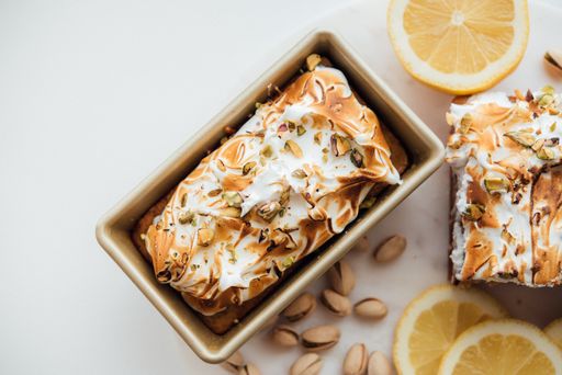 An overhead wide shot of tasty cake dessert with nuts and lemons on a white plate and white background