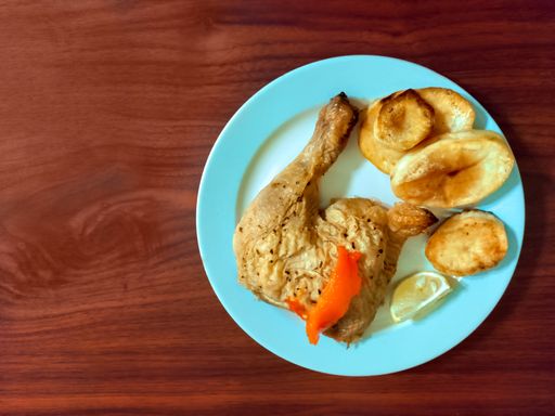 An overhead shot of a traditional cooked chicken leg and roasted Spanish potatoes on a plate on a wooden background