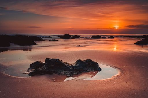 A stunning sunset over a beach with rocks on the sandy shoreline.