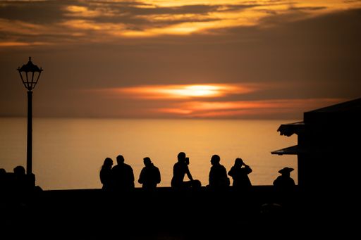 A silhouette of people standing around on a seashore at sunset