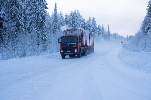 A stunning shot of a big truck passing through a snowy road surrounded by trees