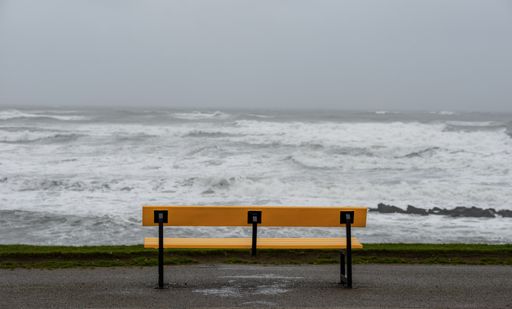 A bench on the beach surrounded by the sea under a cloudy sky during the storm