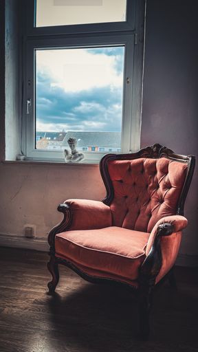 An orange armchair is placed in front of a large glass window, with a statue in front of it