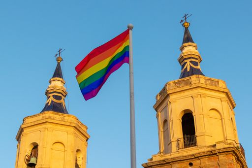 The colorful rainbow flag waving in the wind with the towers of a church on the background