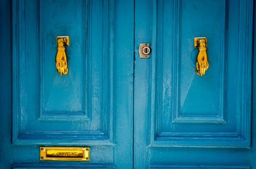 A closeup of an aged vibrant blue door with golden handlers