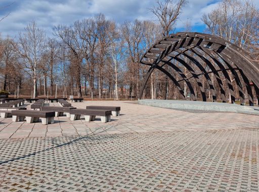 A wooden bench is situated in front of a large open-air structure composed of weathered wooden beams