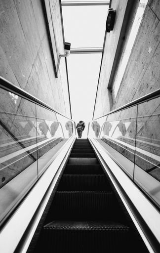 A Low angle shot of a man stepping off a grey metal escalator in a modern building