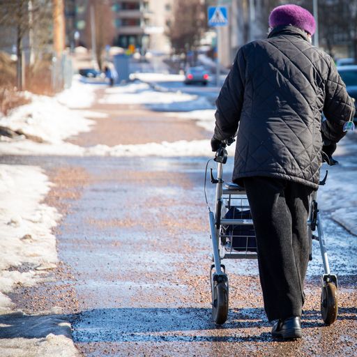 An elderly woman walking with a walker down the snow-covered street