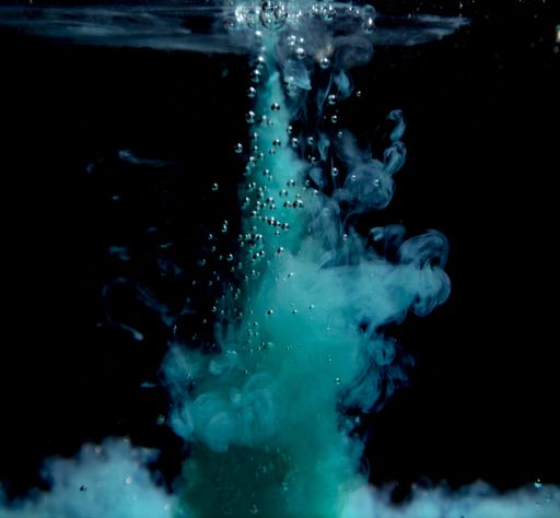 An abstract concept of teal color ink drop plume in water on an isolated  black background