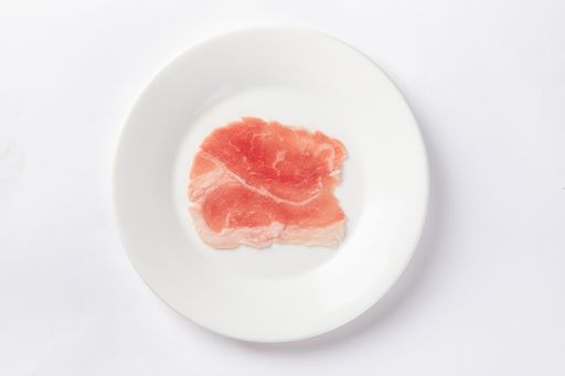An overhead shot of a raw slice of lamb meat on a white plate isolated on white background