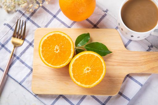 A top view of freshly sliced orange on a wooden chopping board with a fork and cup of coffee