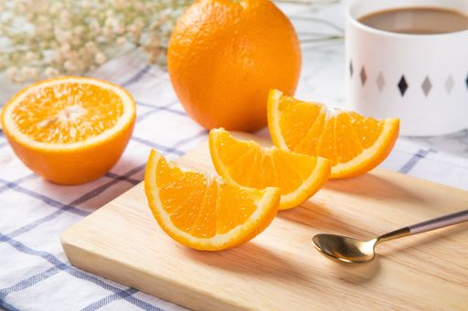 A closeup of cut oranges on a plate on a wooden board on the table with a cup of coffee in the blurry background
