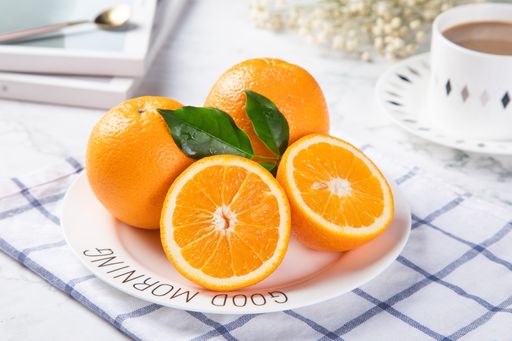 A closeup of fresh oranges on a plate with a cup of coffee beside it