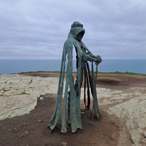 A stone statue of King Arthur perched atop a hill overlooking the vast expanse of the ocean