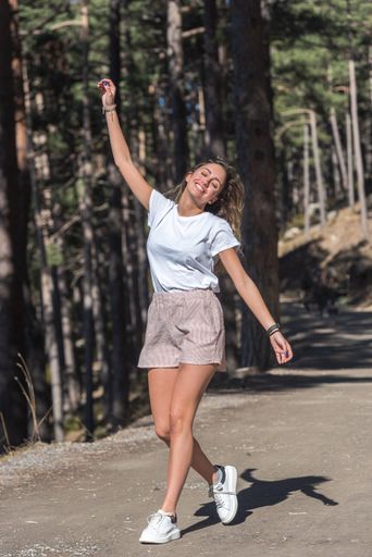 A vertical shot of a happy smiling woman walking down the road with her hands up and down