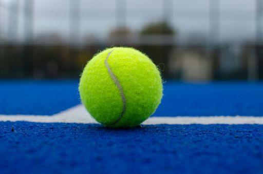close-up view of a ball on the lines of a blue paddle tennis court, racket sports concept