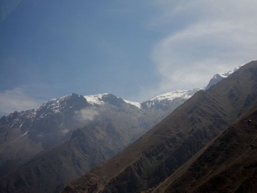 An aerial shot of high rocky snow-capped mountains during sunrise with visible electrical wires