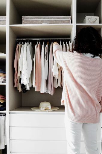 A female is standing in an organized wardrobe with clothes neatly hung on racks surrounding her.
