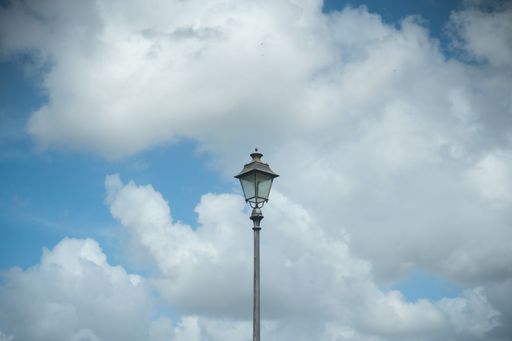 A metal streetlight stands in the city against a backdrop of a vibrant blue sky