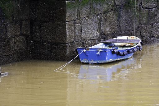 A closeup shot of an old small blue boat on dirty floodwater against a brick wall