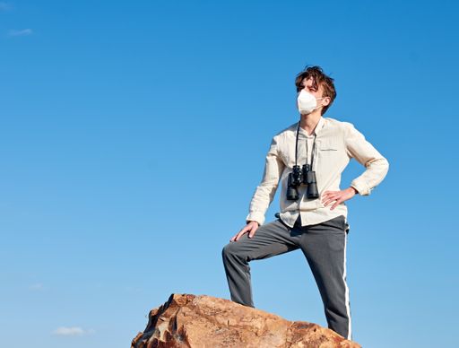 A shallow focus of a confident young man from Spain standing on a cliff wearing a face mask and a white shirt looking into the distance