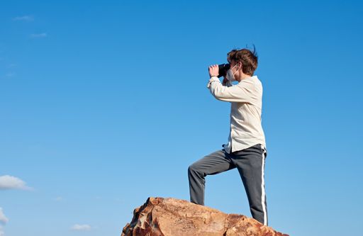 A Spanish adventurous young male traveler standing on a rock wearing a mask and using binoculars