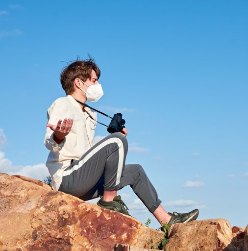 A side view of an explorer from Spain in a mask sitting on a rock surprised by the view