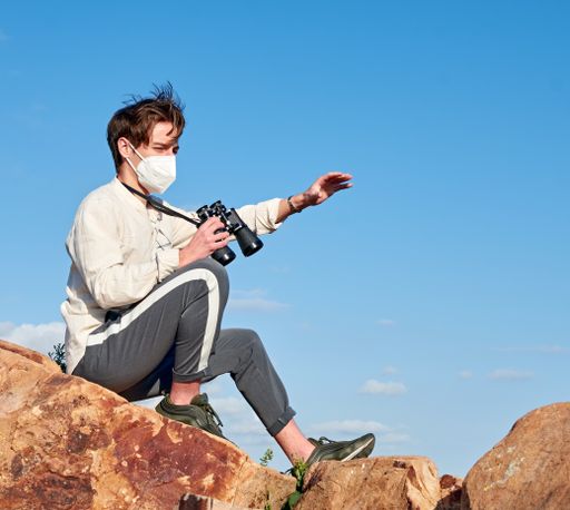 A shallow focus shot of an explorer from Spain with binoculars sitting on a rock wearing a mask