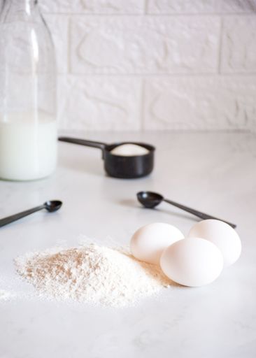 A closeup of a tabletop featuring eggs and flour.
