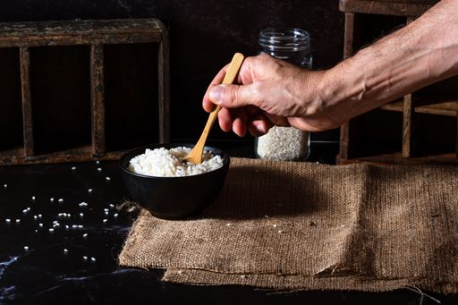 A hand holding wooden spoon to pour rice from a bowl.