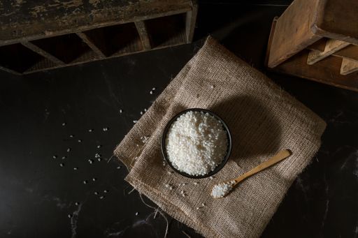 A top view of black bowl and wooden spoon with raw white yamani rice.
