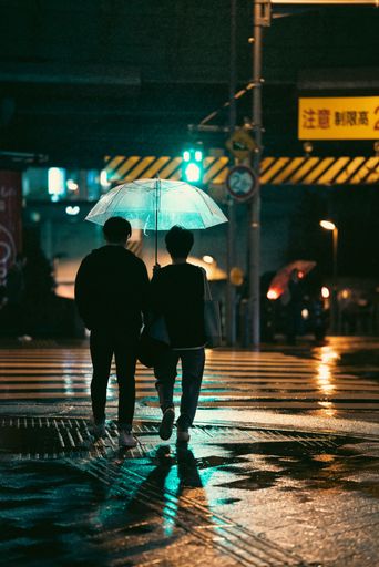 A vertical shot of Two people walking down a city street in the evening during a rainy weather