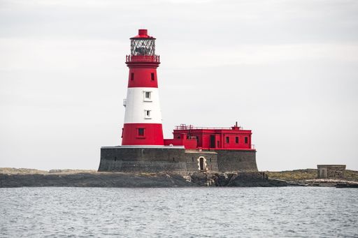 An imposing white and red lighthouse stands tall against a clear sky, its iconic tower reaching up towards the heavens