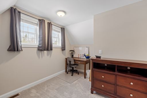 A room with two small windows, a wooden desk and a dresser.