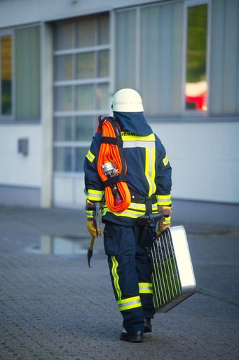 A male fireman walking down a city street carrying a suitcase in his hands