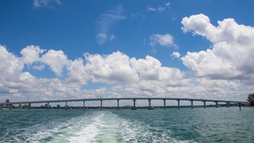 A view of a bridge over a tranquil body of water from the perspective of a boat, with fluffy white clouds in the sky above